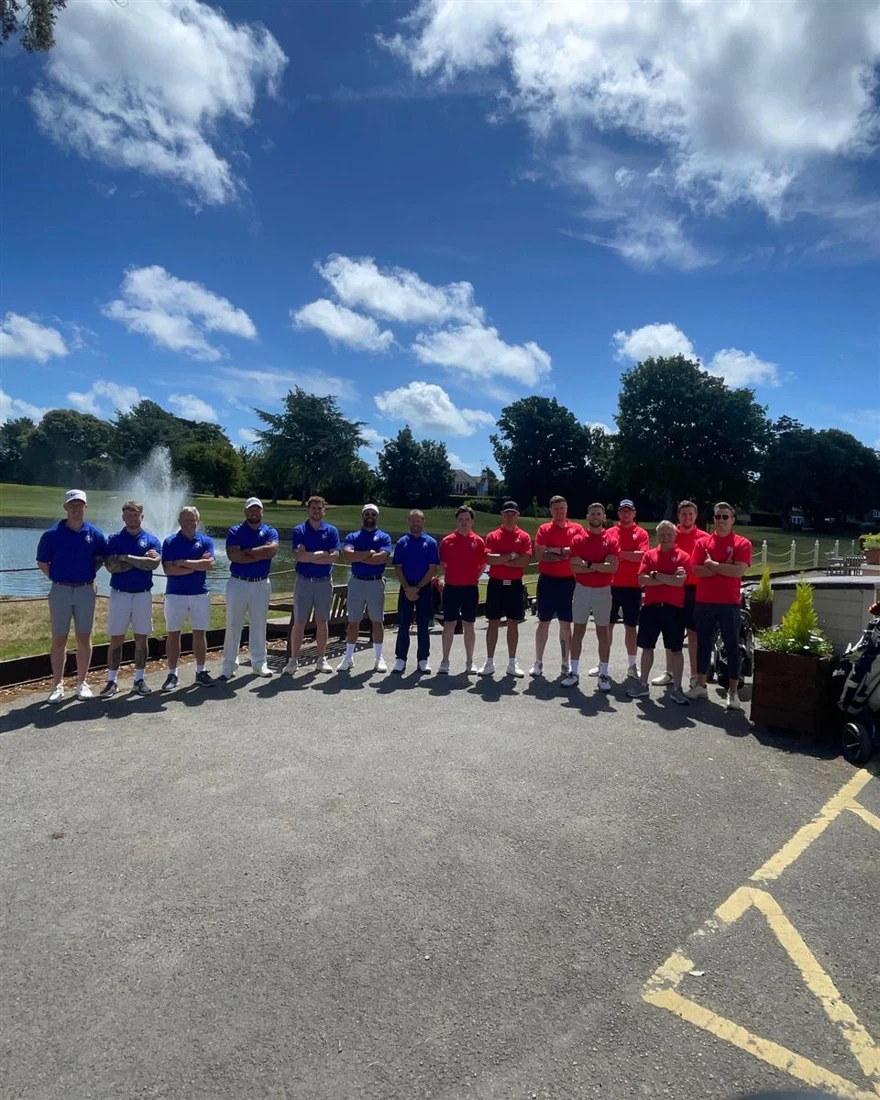 Two teams lined up in blue and red shirts at a lakeside sports day